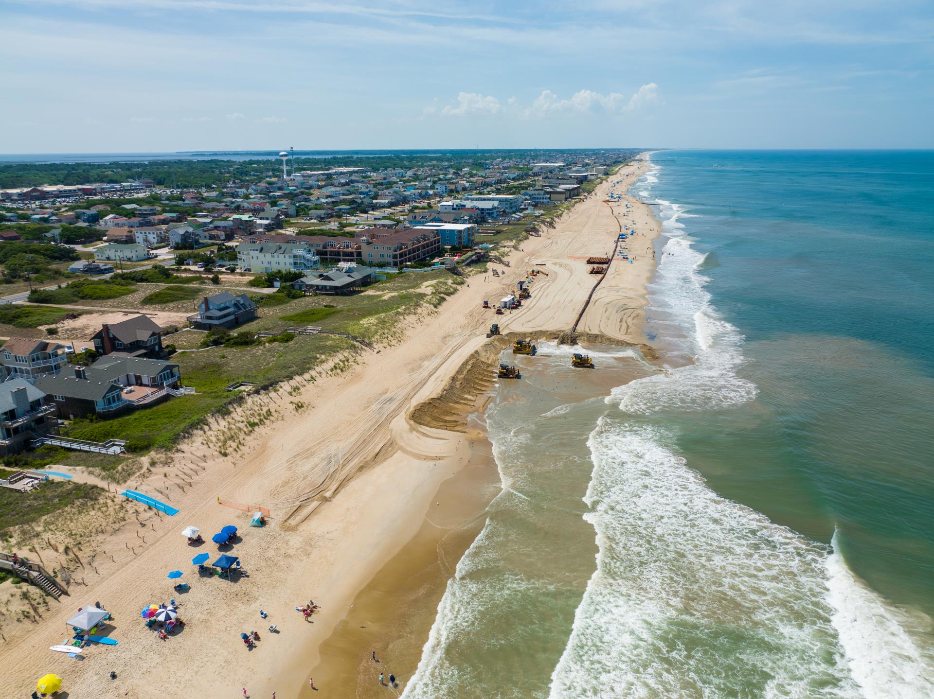Aerial view of Kill Devil Hills beachgoers enjoying the beach while beach nourishment takes places nearby.