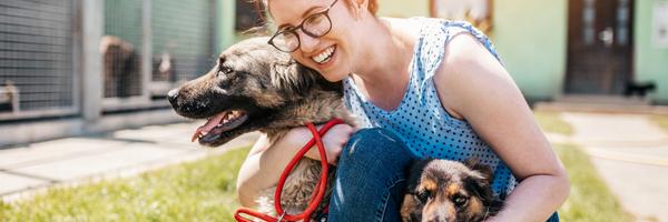 Image of a animal shelter volunteer hugging two dogs.