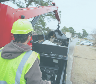 Image of a man operating a crane to deposit large furniture into a dump truck.