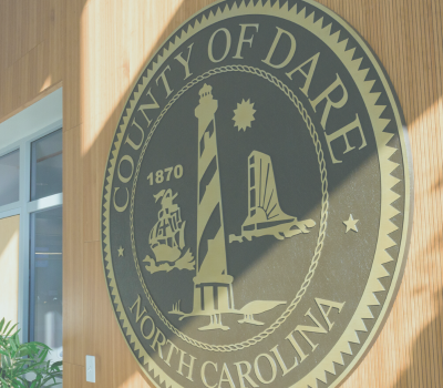Image of a large Dare County seal (logo) hanging on a wooden wall.