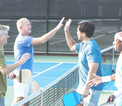 Image of a group of men high-fiving after playing pickleball.