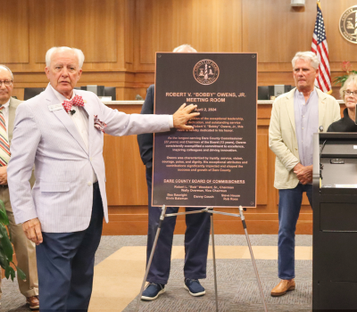 Image of Chairman Woodard referring to a replica of the Bobby Owens room dedication plaque.