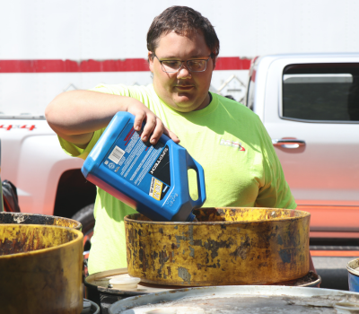 Image of a man in a work shirt safely pouring an old bottle of antifreeze into a metal container.