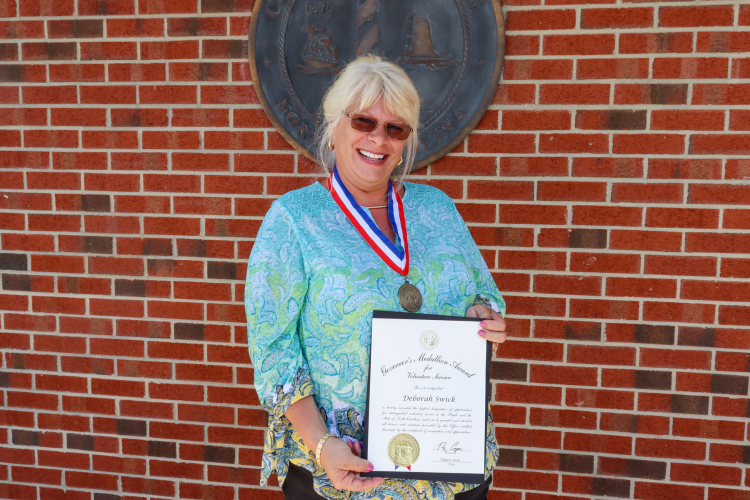 Image of Debbie Swick wearing her medallion and holding her certificate.